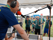 A man wearing headphones operates audio equipment while a group stands behind him.